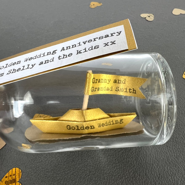 close up of handmade golden paper boat in a bottle, golden wedding anniversary gift
